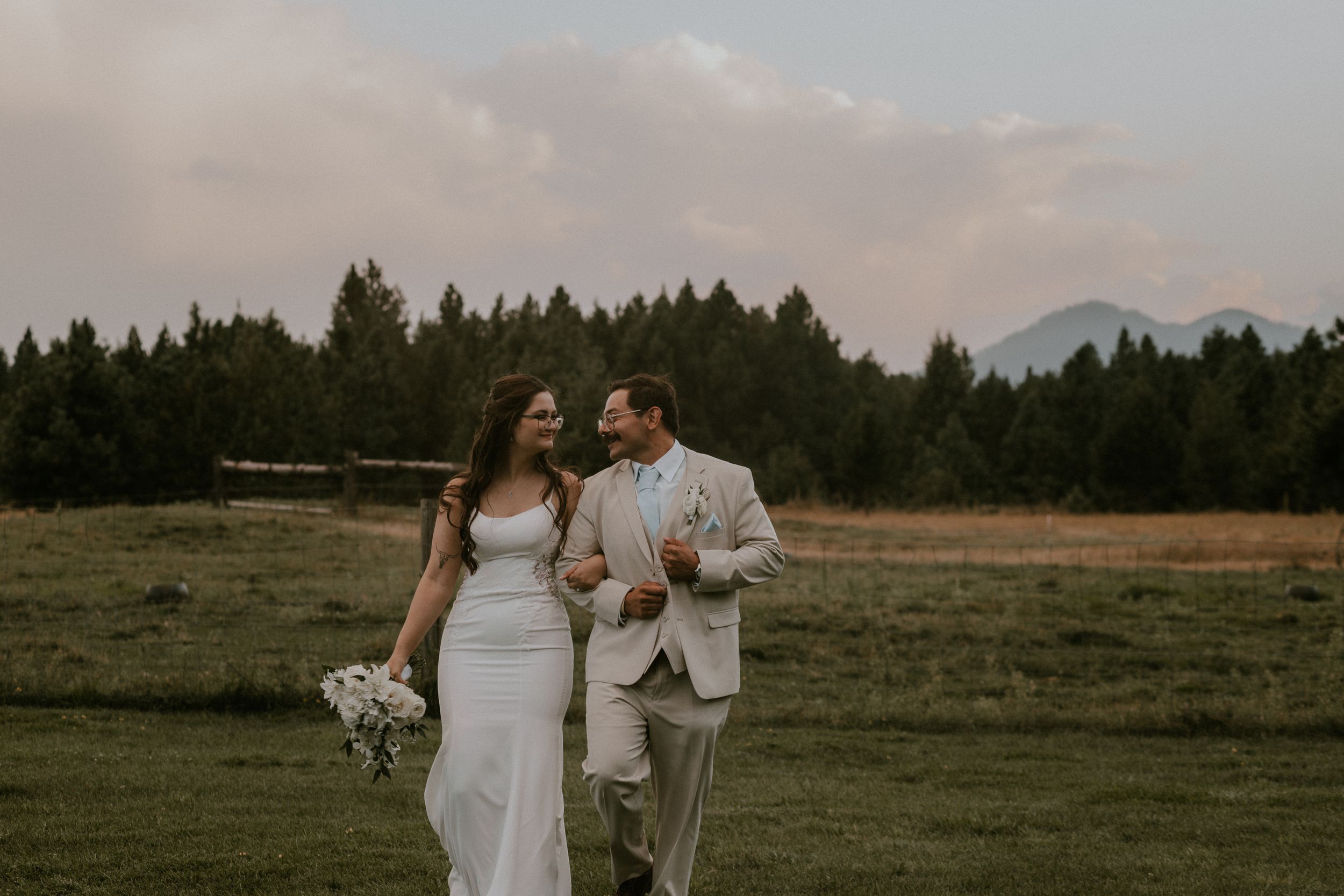 Black and white photo of a bride and groom embracing outdoors, her lace gown flowing in the wind.