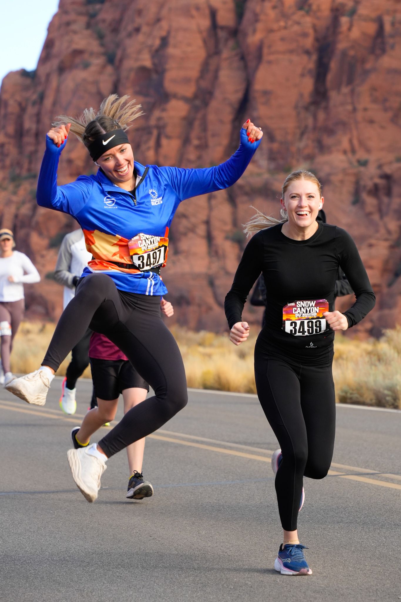 Two women race joyfully in Snow Canyon marathon with red rock formations behind them