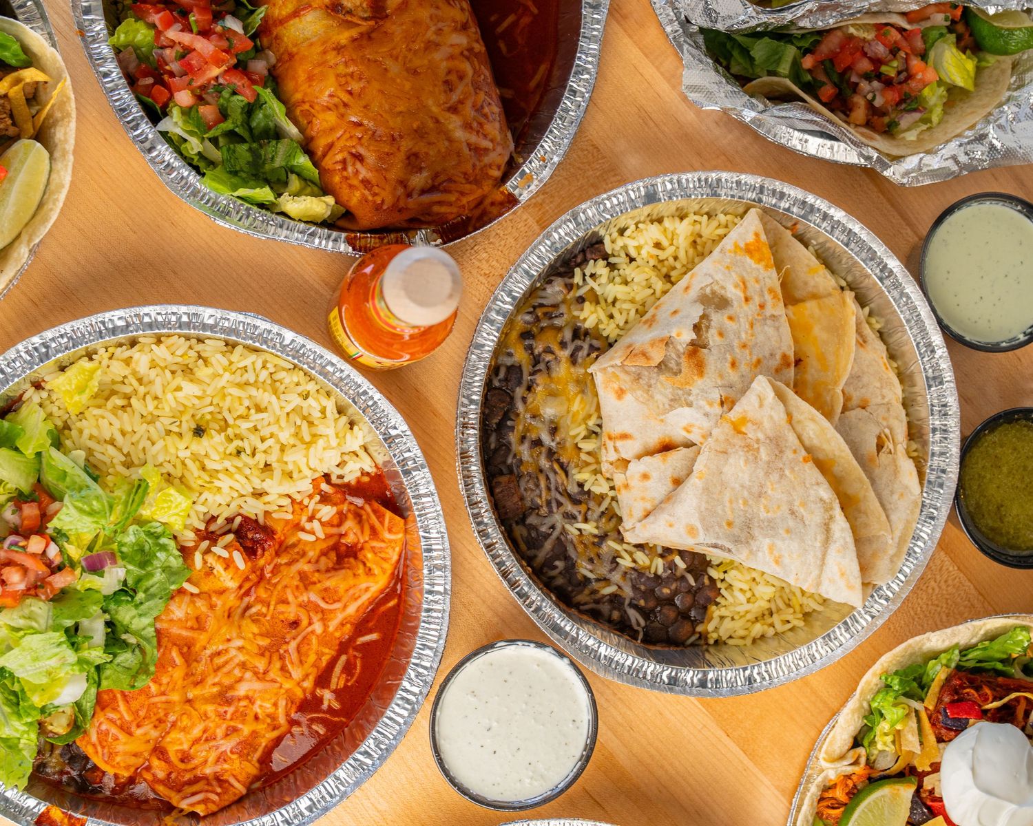 Overhead view of Mexican food spread with enchiladas, rice, beans, quesadillas, and fresh salsa
