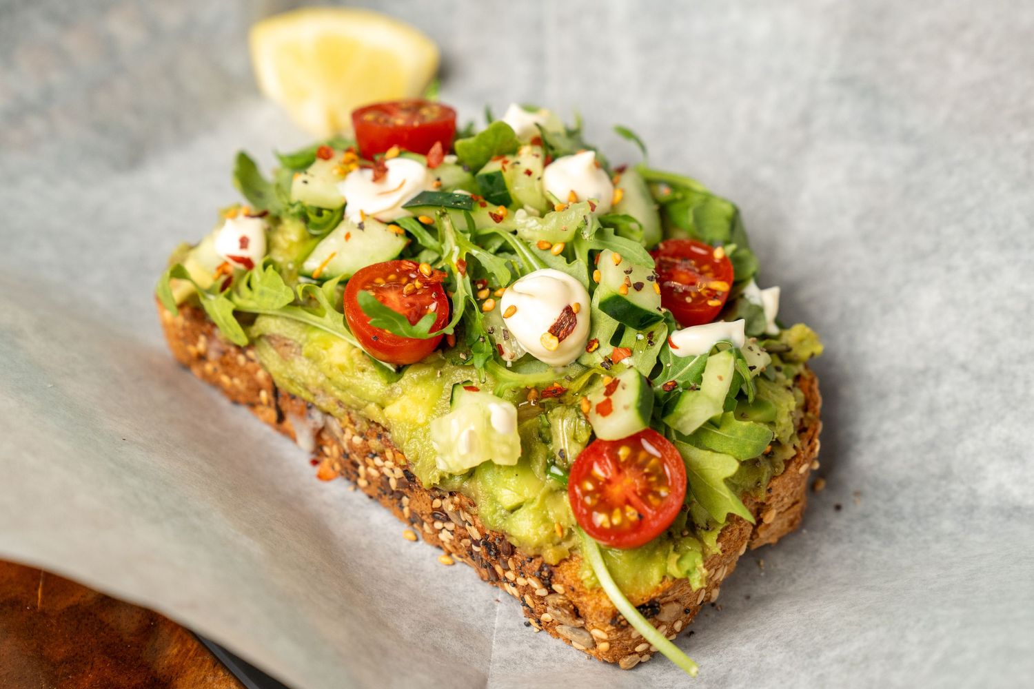 Avocado toast on seeded bread topped with cherry tomatoes, feta cheese, and fresh greens