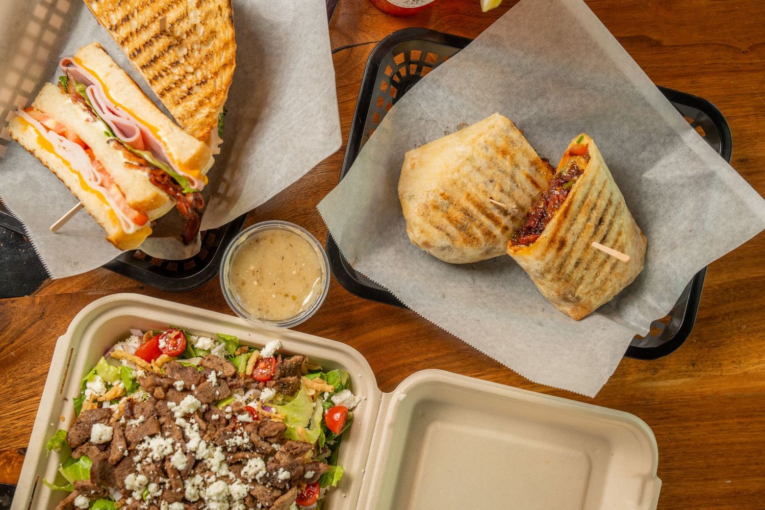 Overhead view of a panini sandwich, burrito wrap, and Greek salad with feta cheese