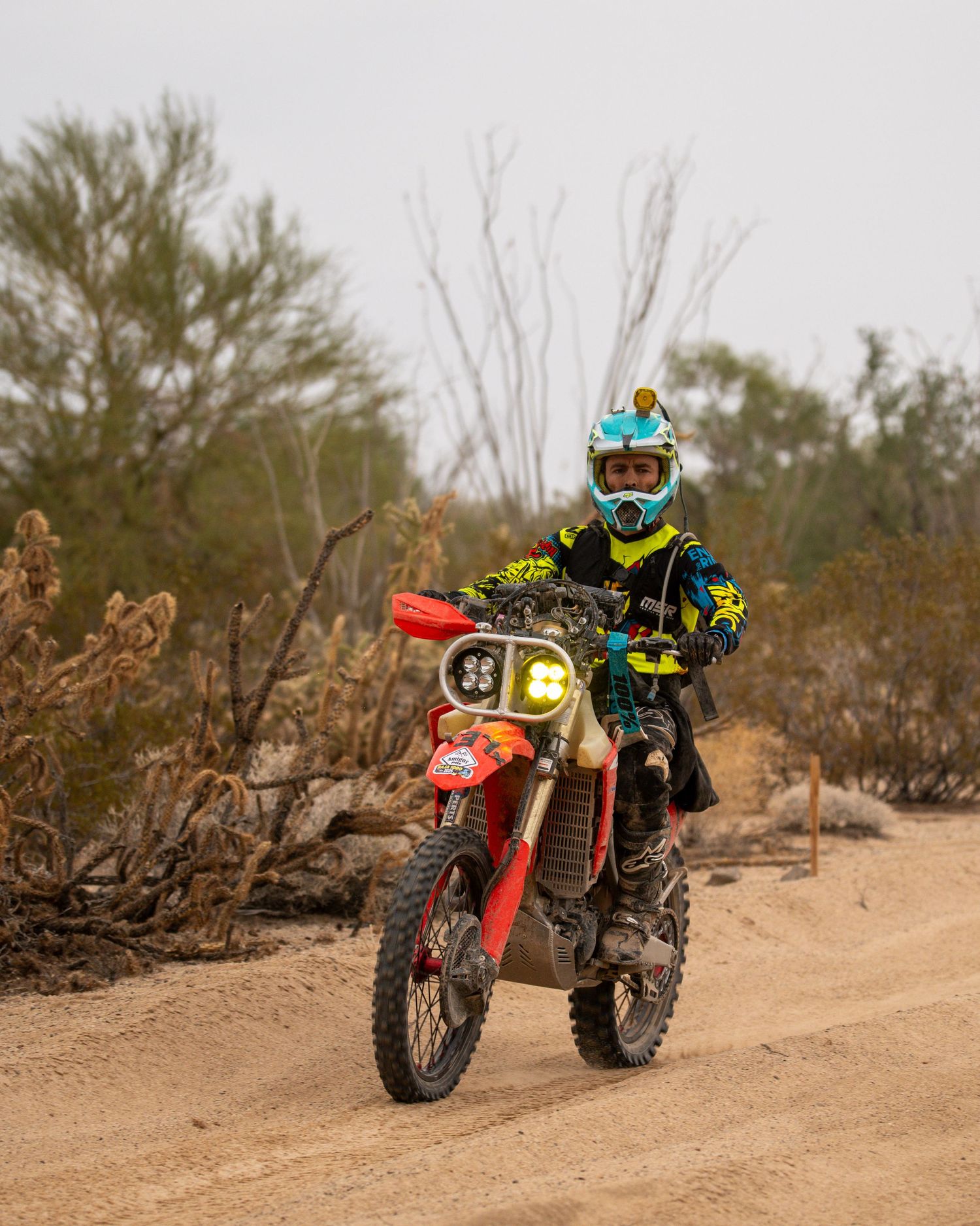 Dirt bike rider in colorful gear navigating a sandy desert trail