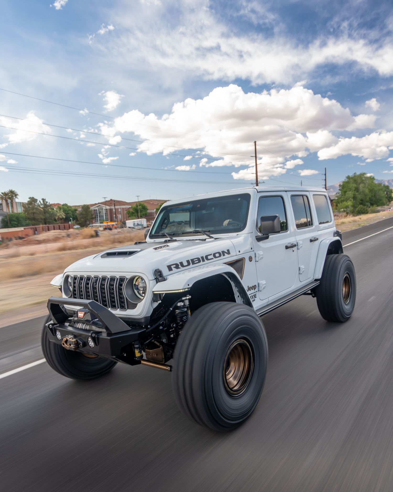 White Jeep Wrangler Rubicon with oversized off-road tires driving on a desert highway