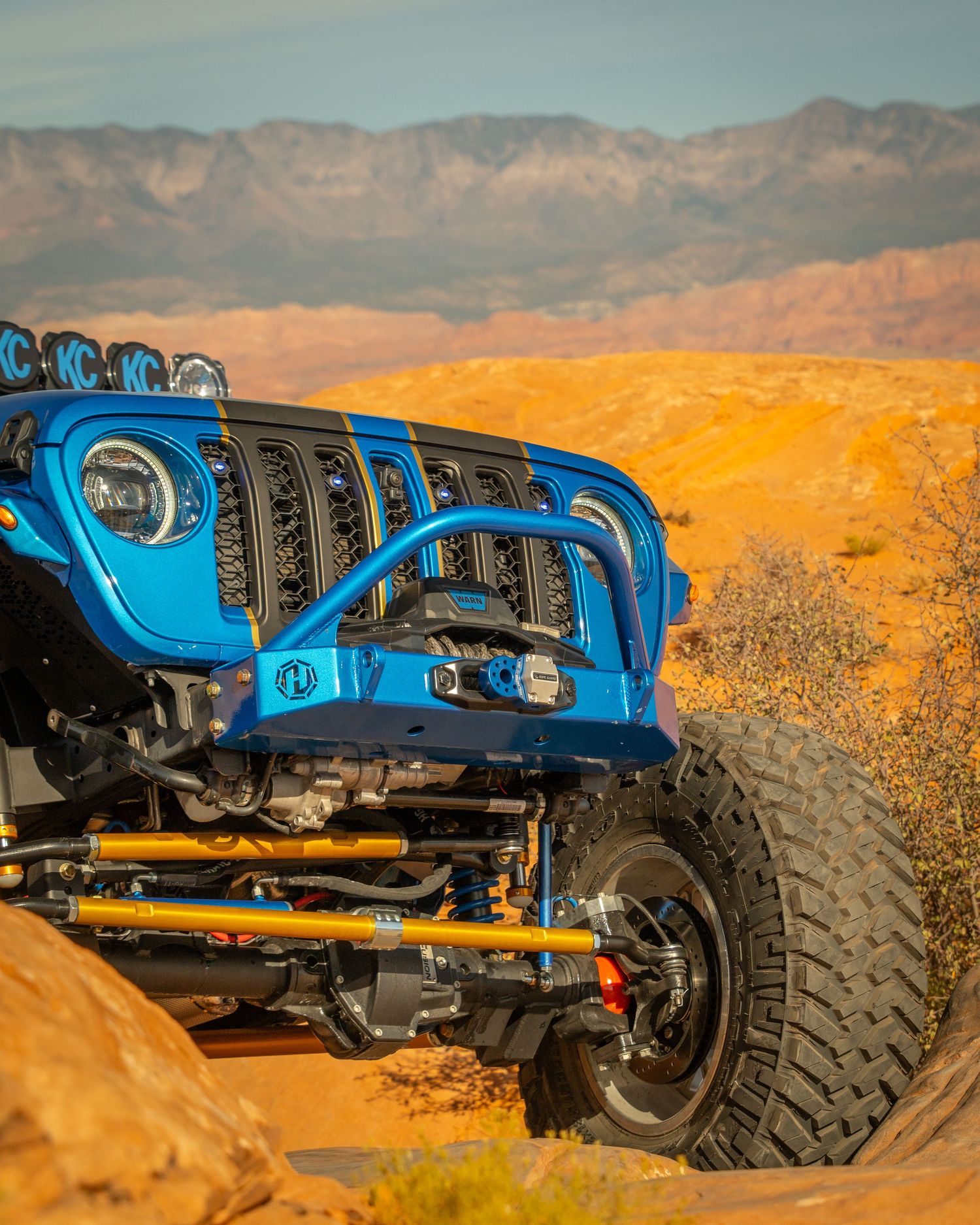 Blue Jeep Wrangler with LED lights and gold suspension components on rocky desert terrain