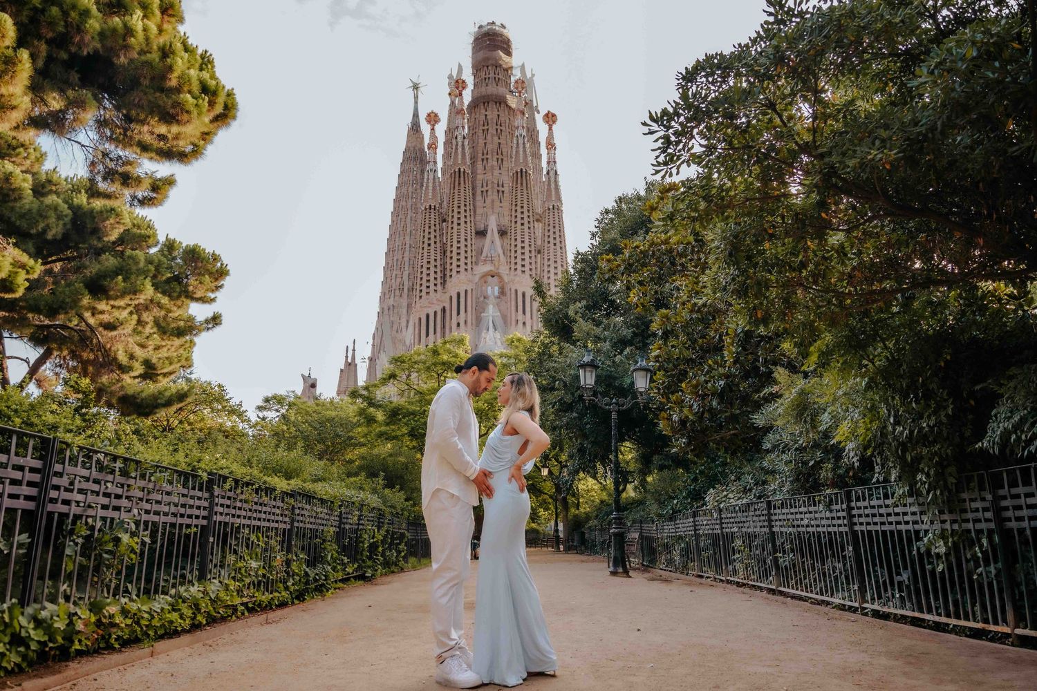 A husband gently kissing his wife's forehead during their maternity photoshoot in a quiet, classic city square.