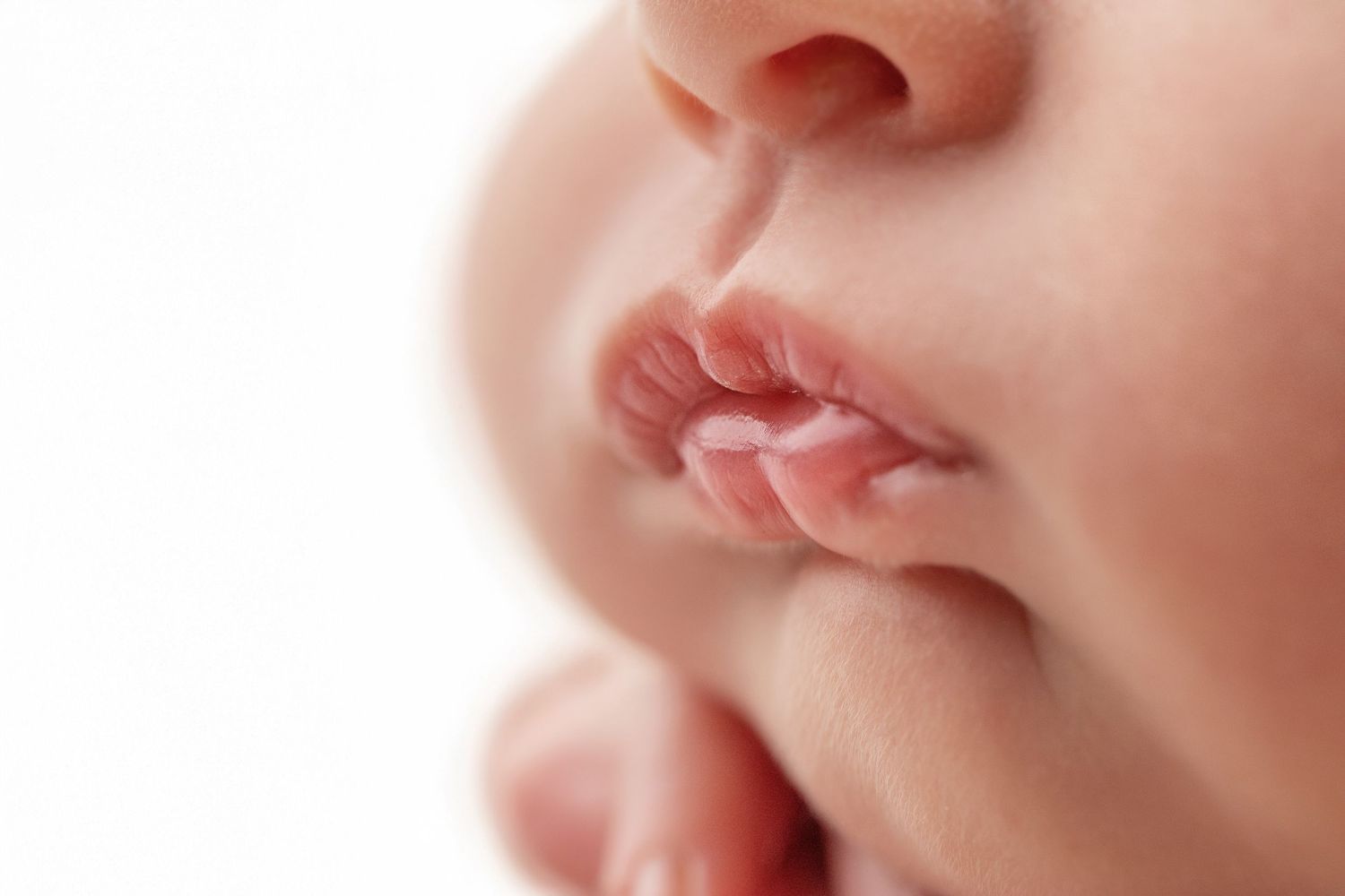 Close-up of a newborn baby's delicate pink lips and tiny fingers against a white background.