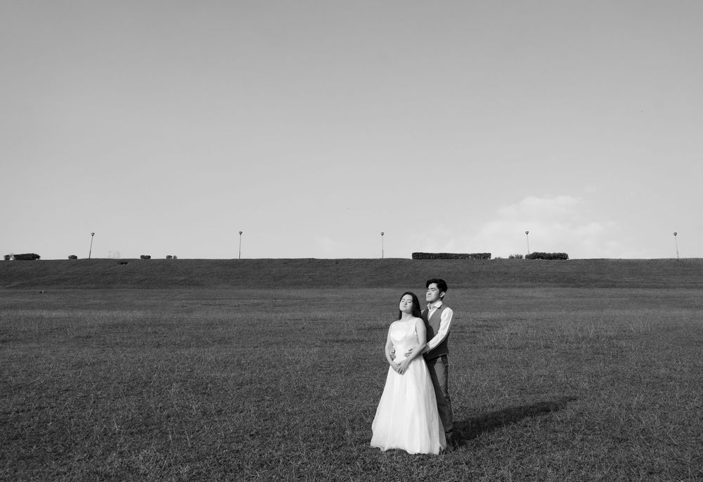 Black and white photo of a bride and groom standing in a vast open field with a clear sky backdrop.
