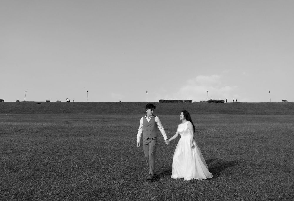 Black and white photo of a bride and groom holding hands in an open field on their wedding day.