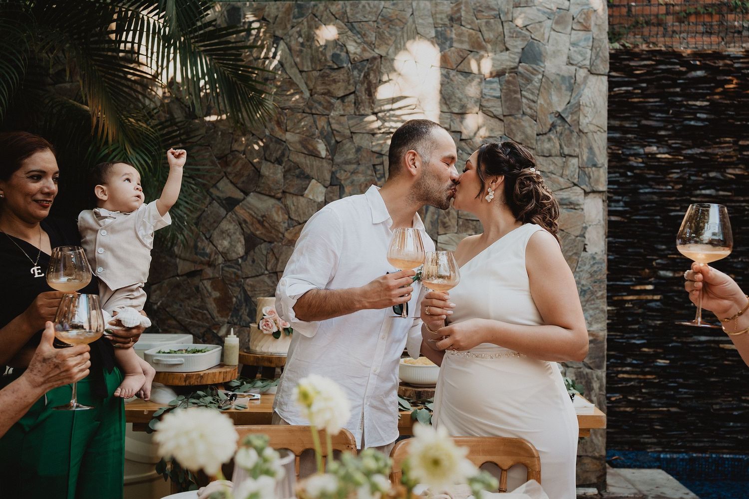 Los novios se besan durante el brindis rodeados de sus seres queridos.