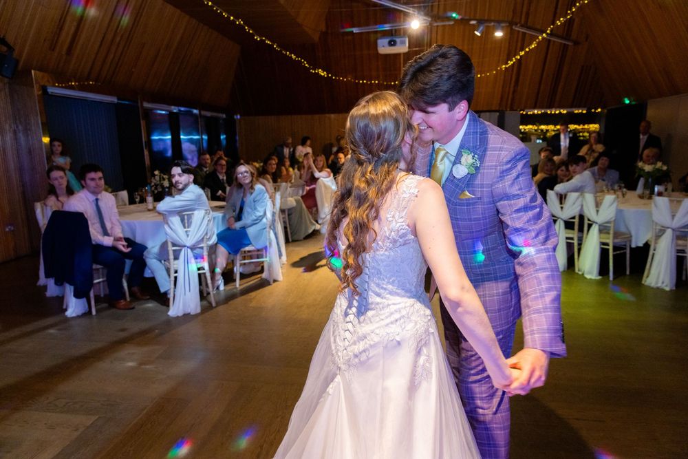 Bride and groom share their first dance at a wedding reception in a warmly lit wooden venue.