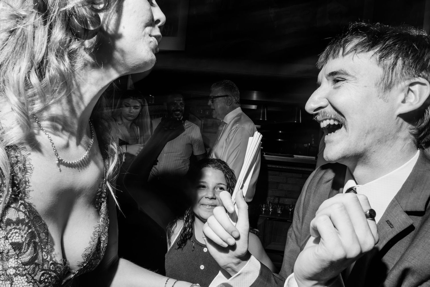 Black and white photo of a man and woman laughing together at a party, with a child watching in the background.