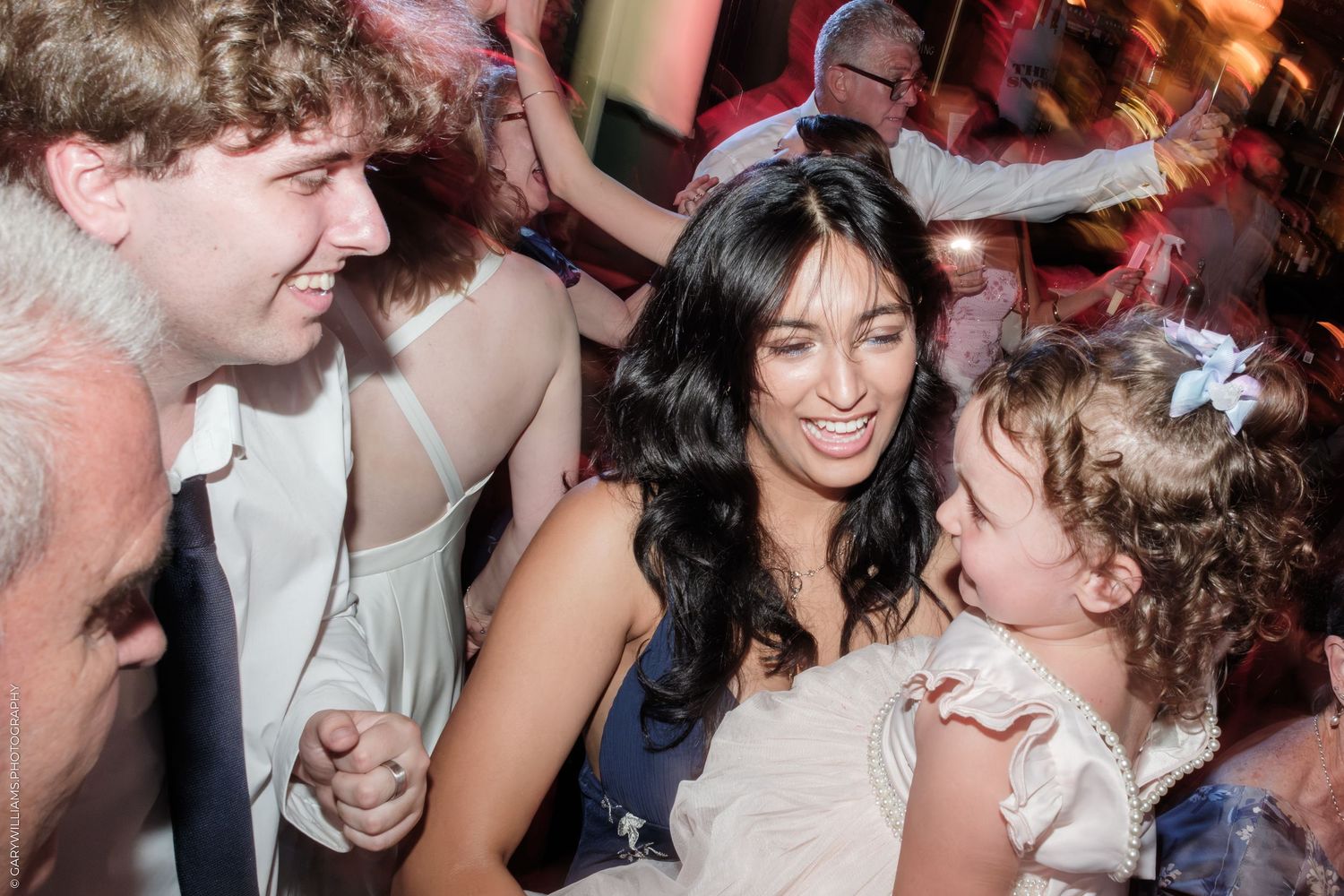 Adults and a young girl in a white dress share a joyful moment together at a festive celebration or wedding reception.