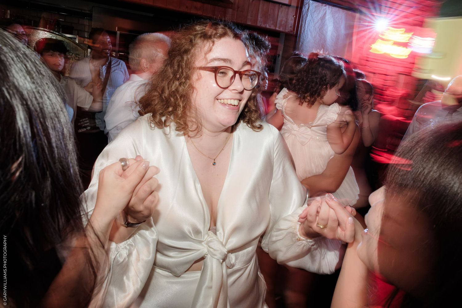 Woman in white satin dress dancing joyfully at a wedding reception party.