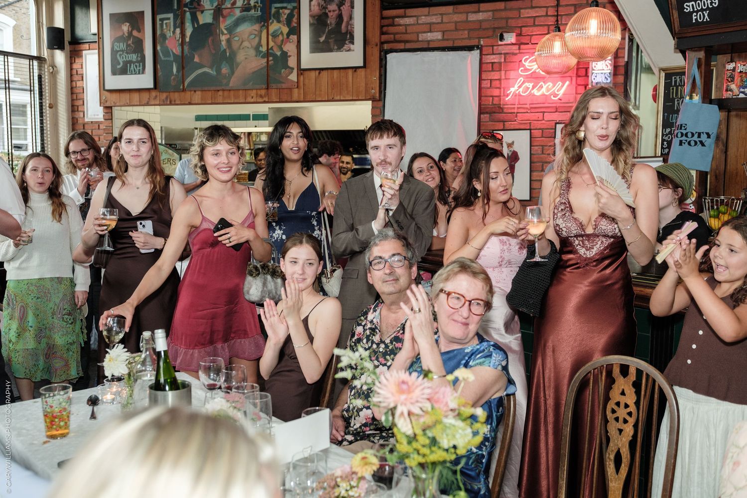 Guests in formal attire react emotionally at an indoor wedding reception in a decorated restaurant venue.