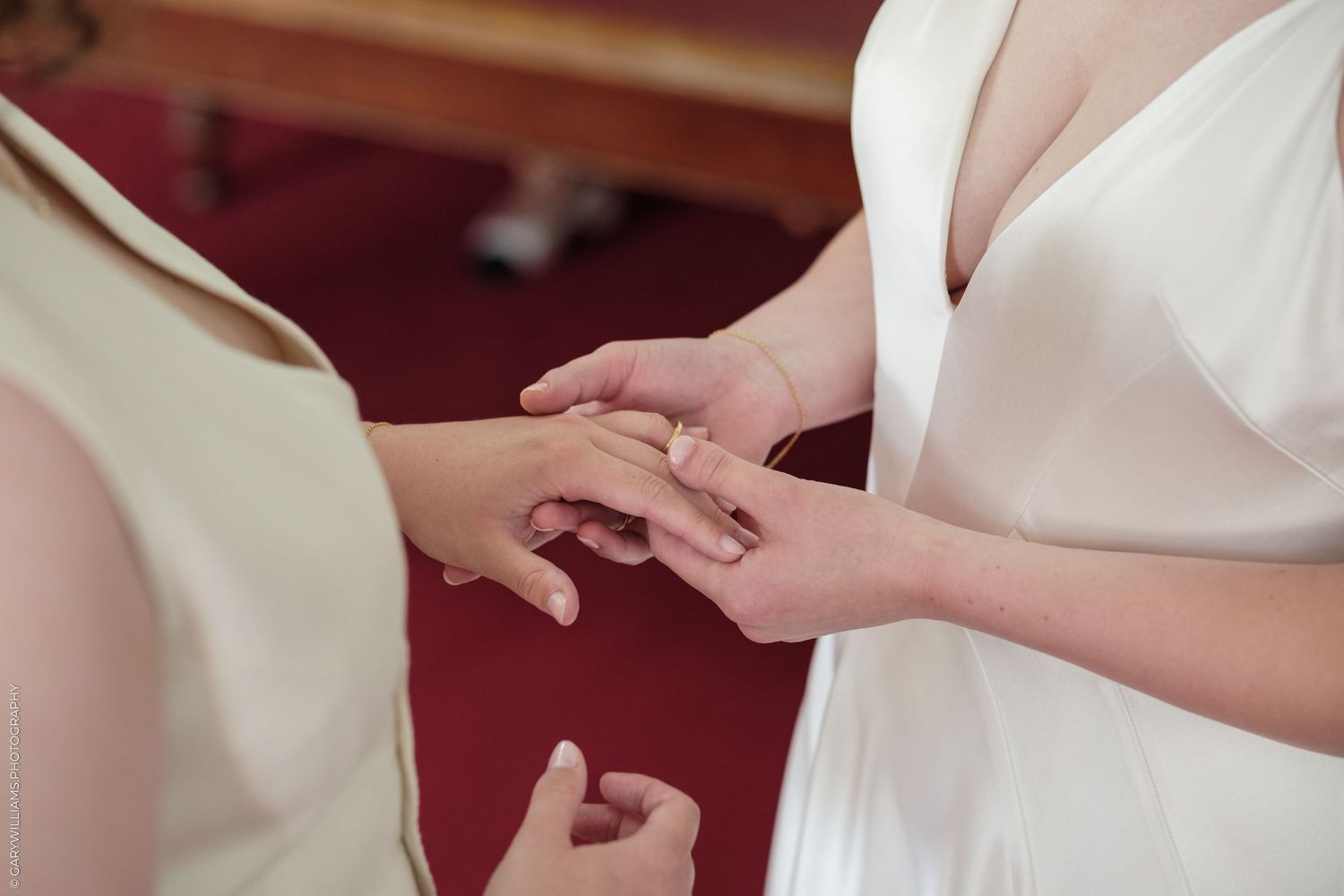 Two brides exchanging wedding rings during a ceremony, wearing elegant white gowns in a church setting.