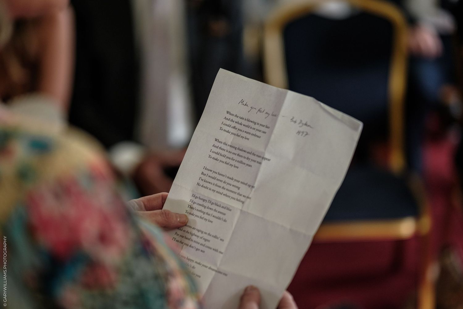 Person holding a wedding ceremony program booklet at an elegant venue with blue chairs in the background.