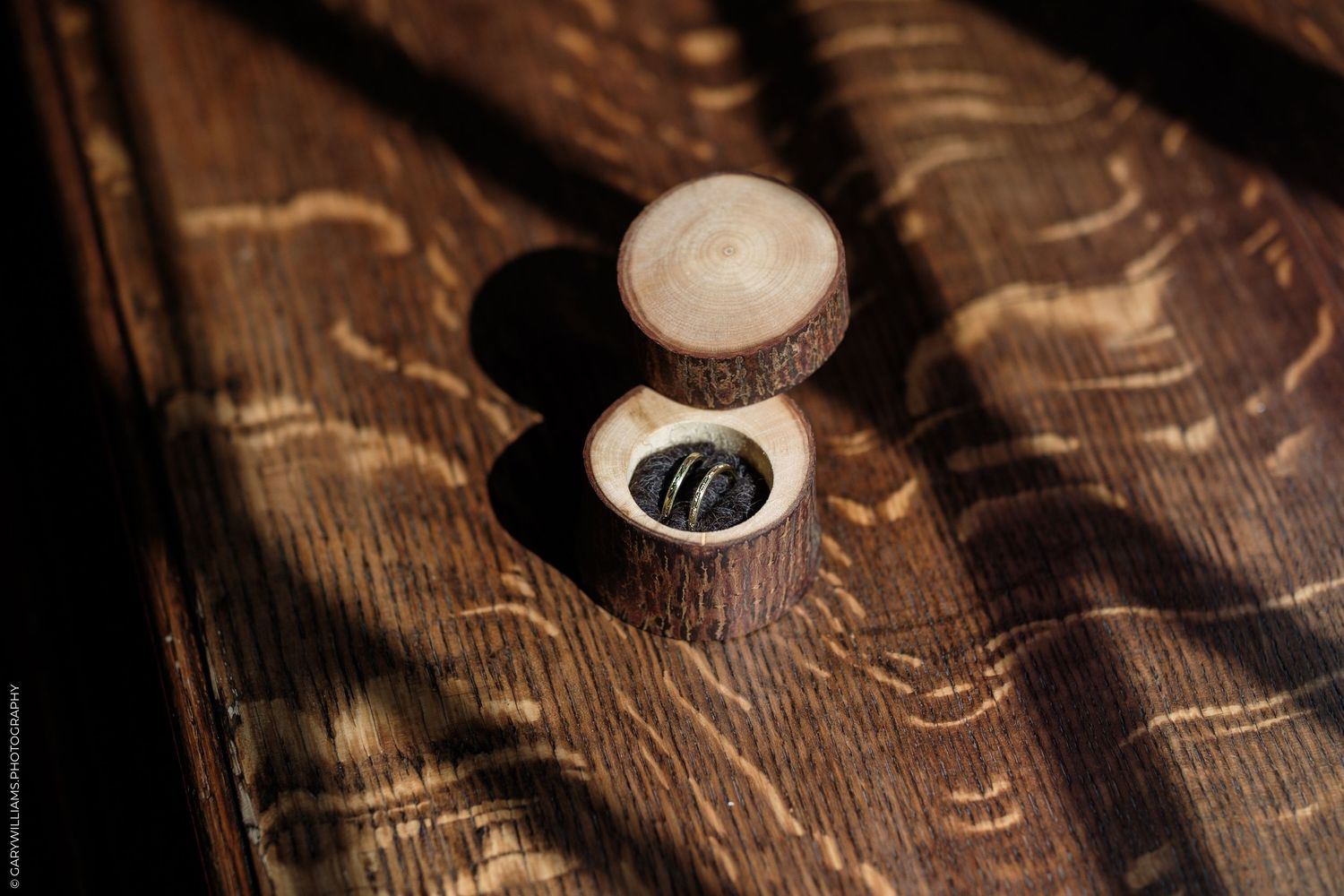 Rustic wooden ring box open on a dark wood surface, holding a dark ring in soft natural light.