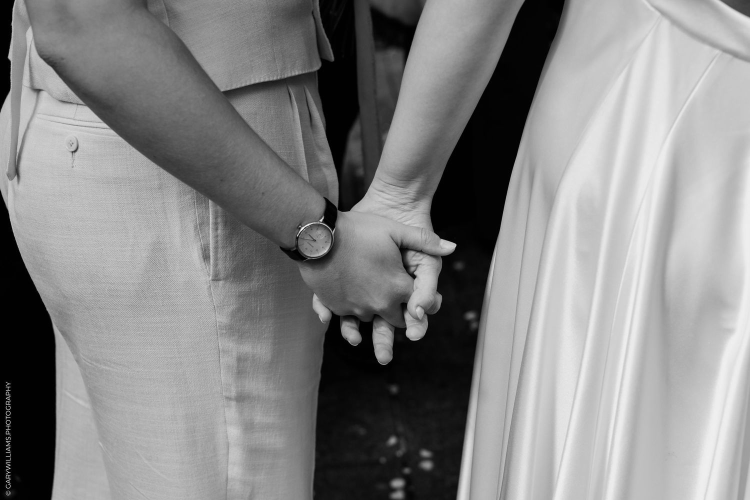 Black and white photo of a couple holding hands, one wearing a watch, dressed in wedding attire.