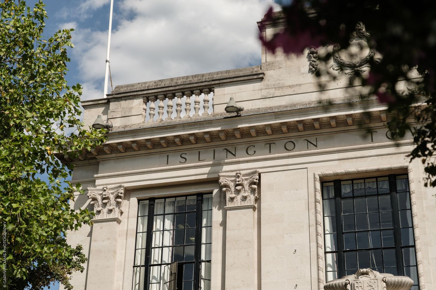 Islington Council building facade with classical stone architecture, large windows, and surrounding trees under a blue sky.