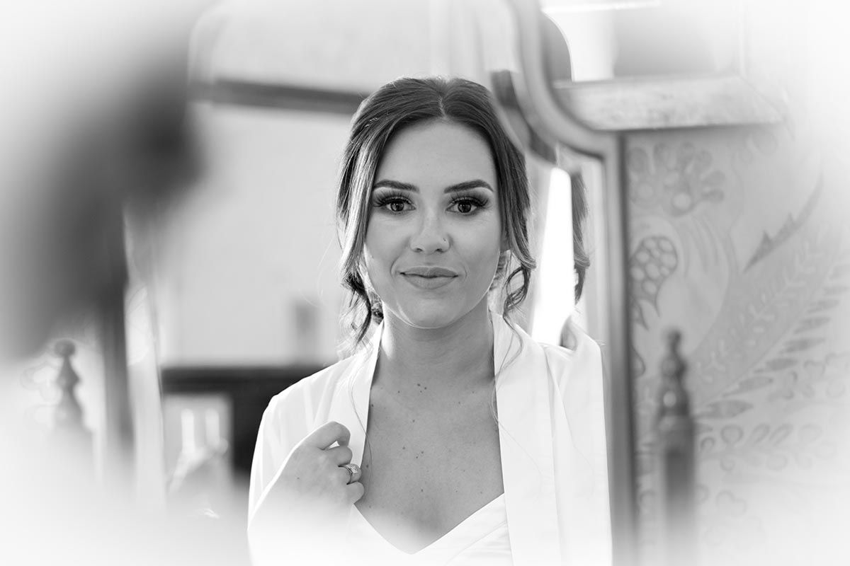 Black and white portrait of an elegant bride in a white robe, wearing drop earrings, gazing softly at the camera.