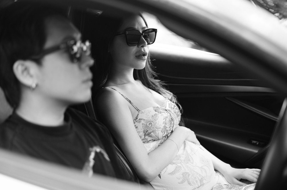 Black and white photo of two people wearing sunglasses sitting inside a luxury car.
