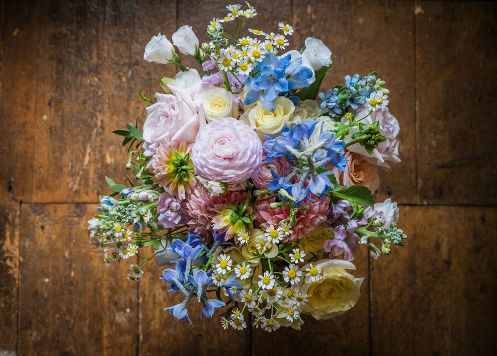 Overhead view of a romantic wedding bouquet with pink roses, blue hydrangeas, and wildflowers.