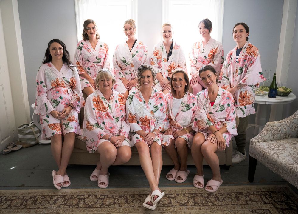 Bridesmaids wearing matching floral robes posing together in a bright room before the wedding.