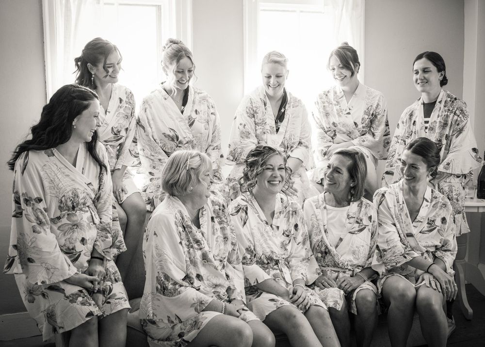 Bridesmaids laughing together in matching floral robes during wedding preparations in a bright room.