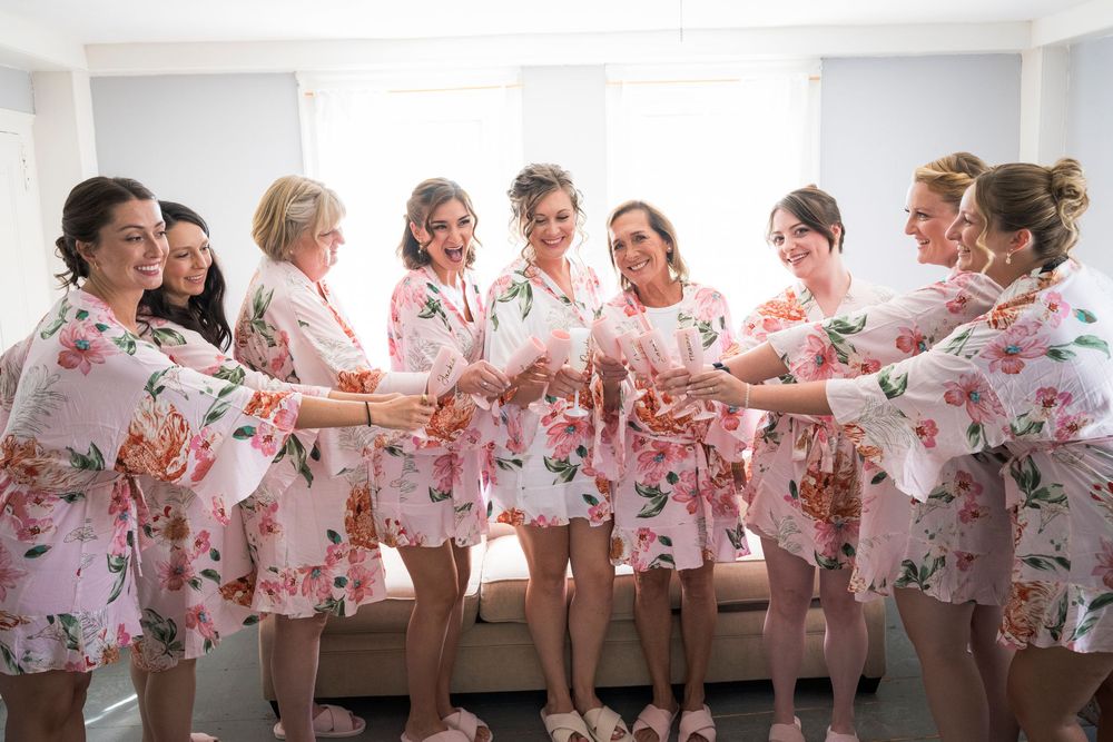 Bridesmaids in matching floral robes toasting together during wedding morning preparations.