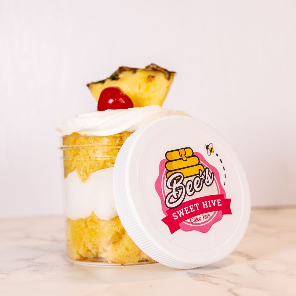 Dessert in clear container with pineapple and cherry garnish next to Sweet Hive branded lid.