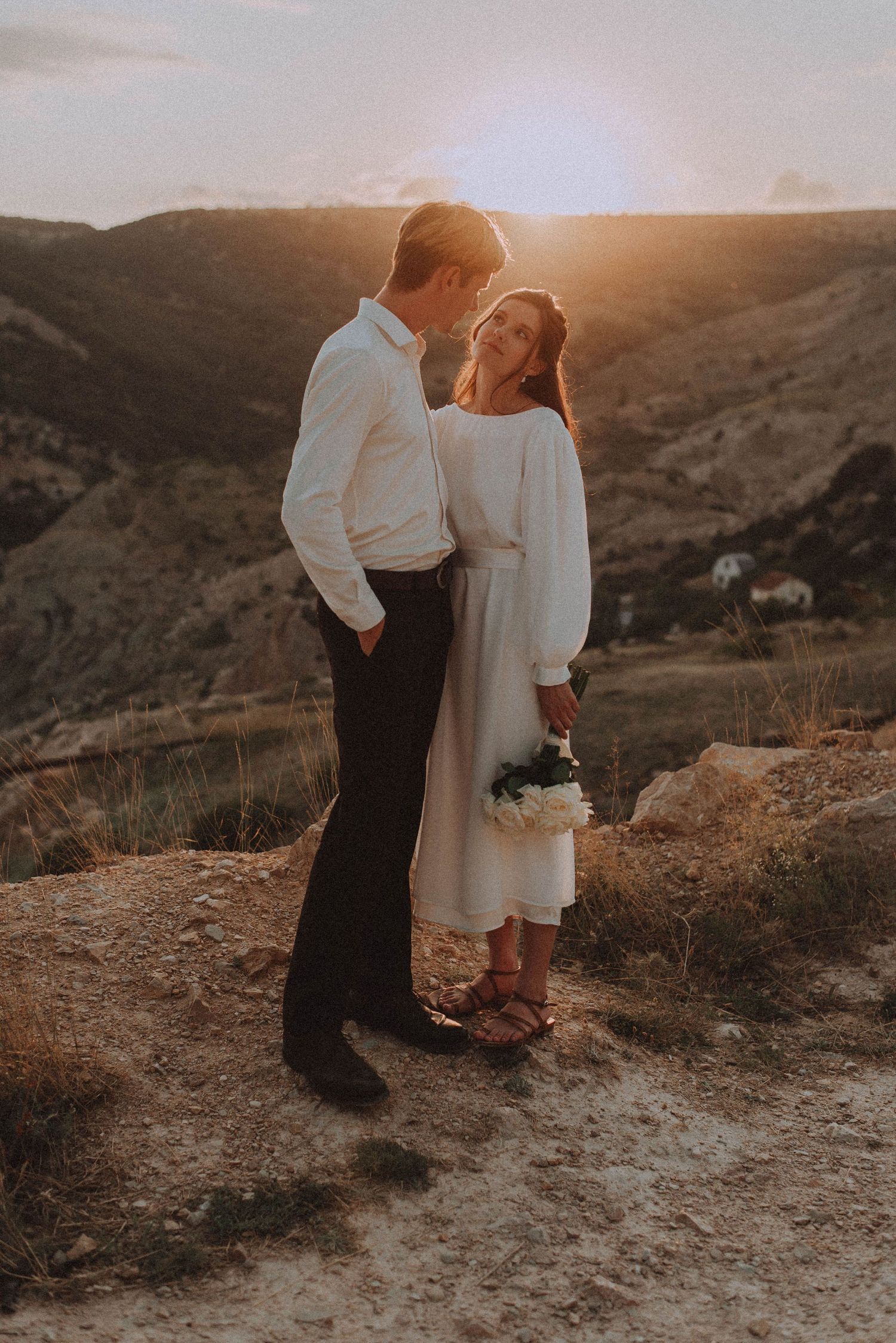 Couple in wedding attire sharing a romantic moment at golden sunset overlooking a scenic mountain valley.