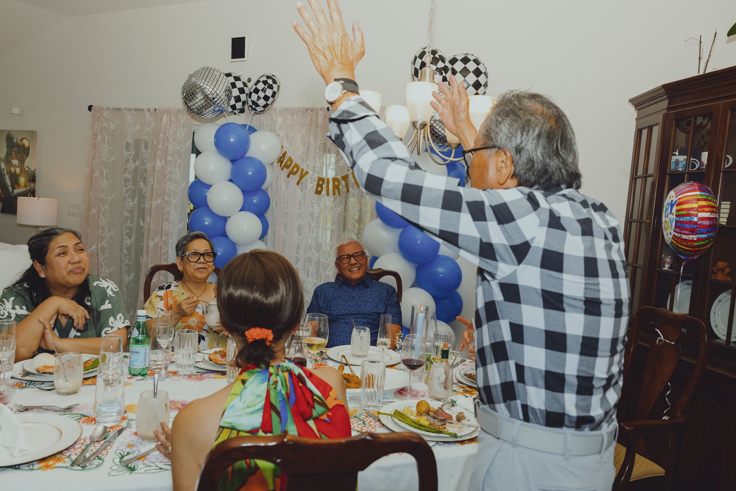 Guests celebrate at a birthday party with blue and white balloon decorations and a Happy Birthday banner.