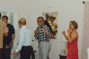 People socializing at an indoor art gallery event with a golden sculpture painting displayed on the wall.
