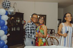 Couple smiling and embracing at a festive party with blue and white balloon decorations indoors.