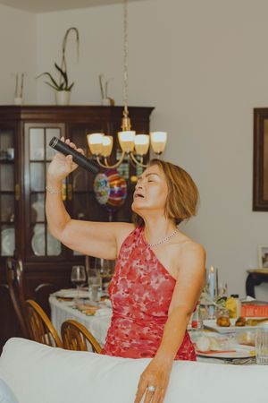 Woman in red floral dress singing karaoke with microphone at elegant dinner party setting.