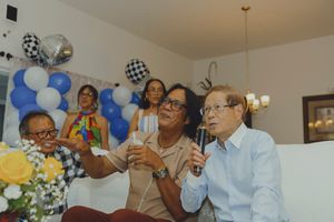 Elderly couple toasting drinks at a festive party with blue and white balloon decorations.