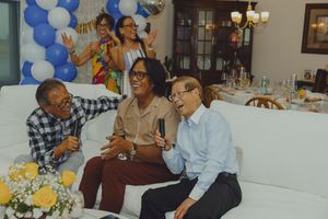 Friends laughing together on a white sofa at a festive blue and white balloon birthday party celebration.