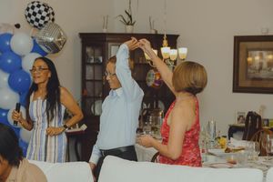 People celebrating at a party with blue balloon decorations, a disco ball, and guests dancing near a festive dining table.