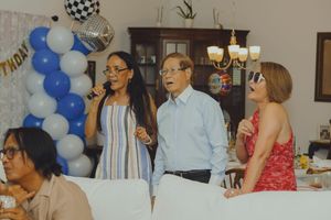 Group of people singing karaoke together at an indoor birthday party with blue and white balloons.