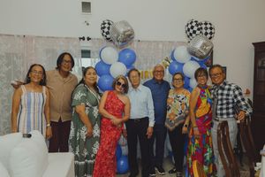 Group of eight people posing together in front of a blue balloon arch at a birthday celebration.