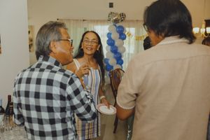 Adults socializing at a festive indoor party with blue balloon decorations in the background.