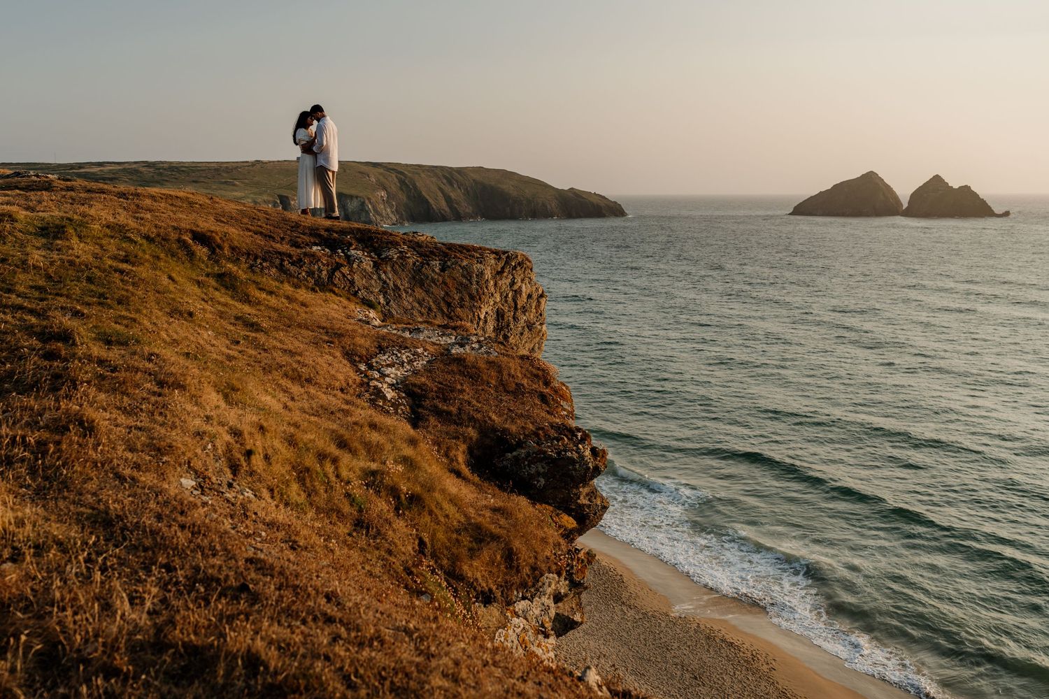 Couple standing on dramatic coastal cliffs overlooking gul rocks at Holywell Bay in cornwall.
