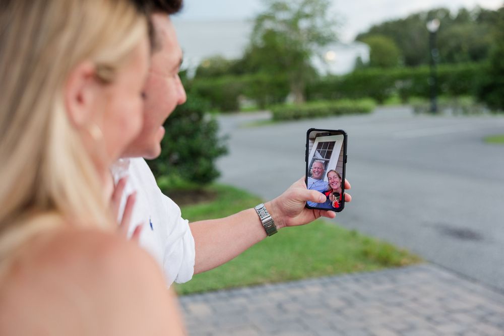 Woman taking a selfie on a smartphone outdoors, displaying the photo on screen while standing near greenery.