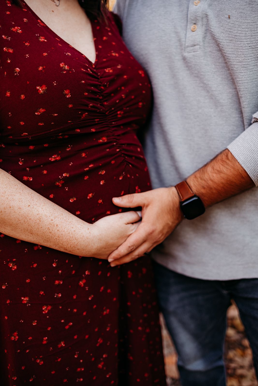 A couple standing each other and they are both holding each others hand on the expectant mothers belly.