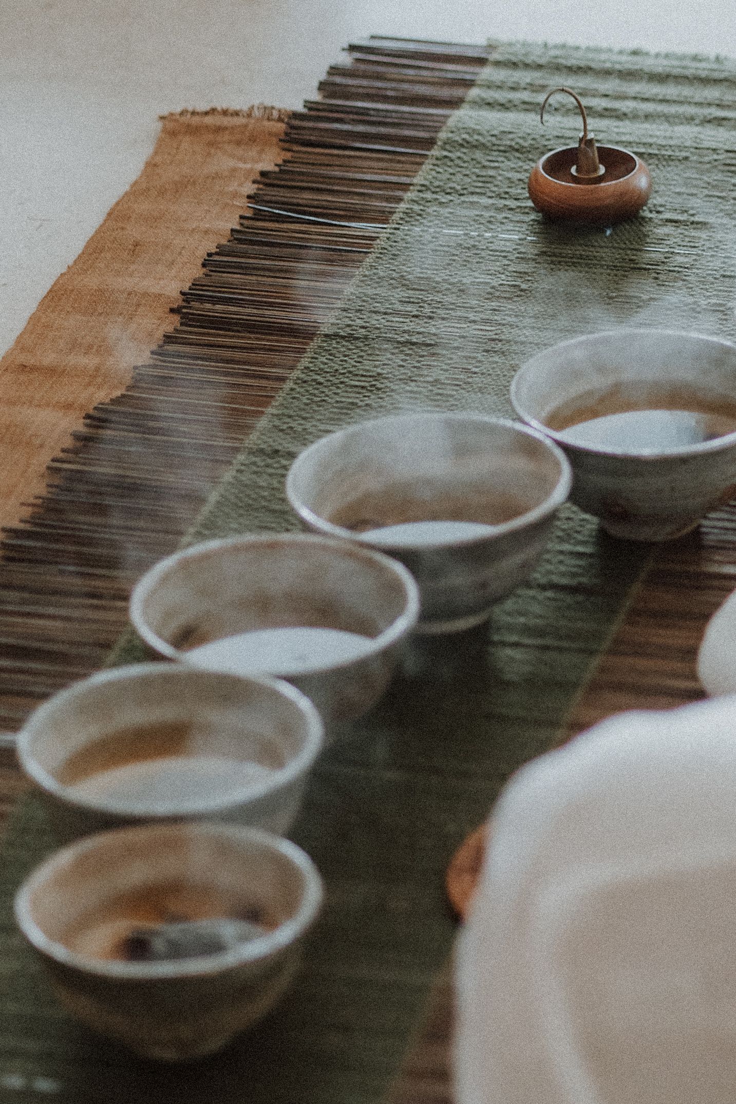 Rustic ceramic tea bowls arranged in a row on a woven mat with a small incense burner during a traditional tea ceremony.