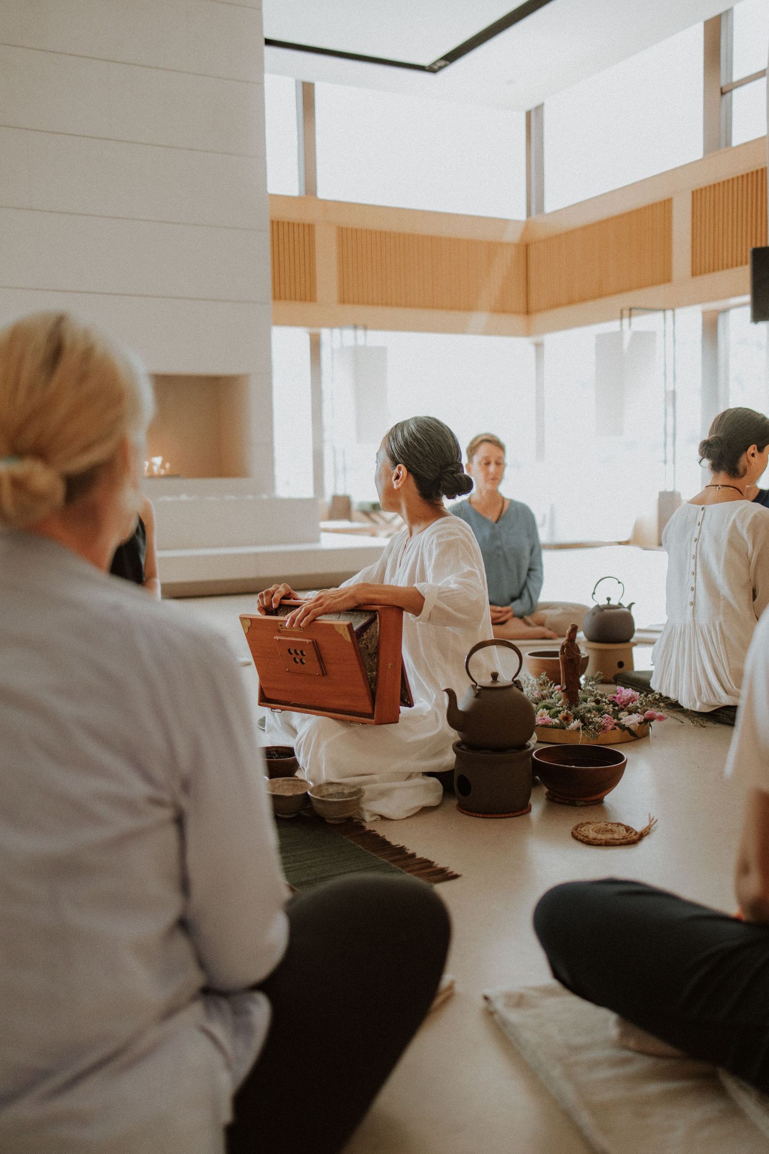 A serene Japanese tea ceremony with participants seated on the floor in a bright, modern minimalist space.