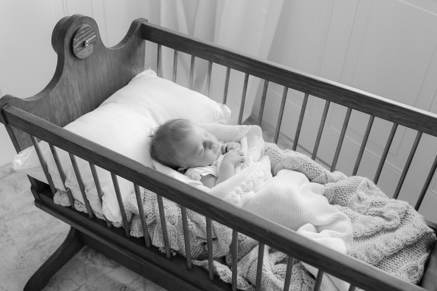 Black and white photo of a sleeping newborn baby in a wooden cradle with soft blankets.