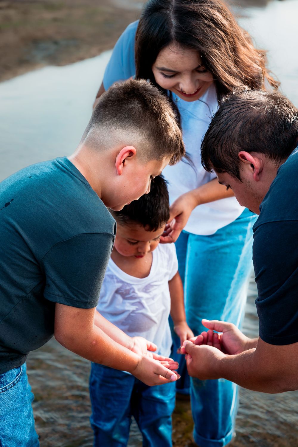 Family of four examining small treasures in their hands near a peaceful waterway outdoors.