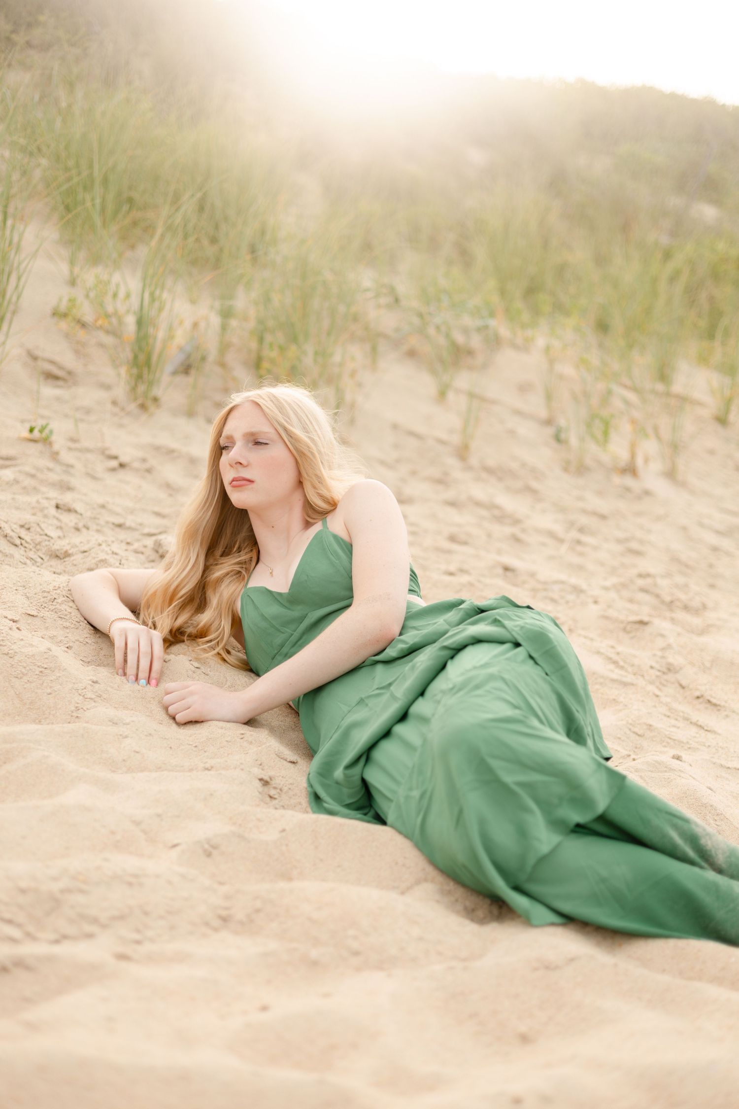 Young woman in white dress sitting on sandy beach, smiling warmly with ocean waves in background.