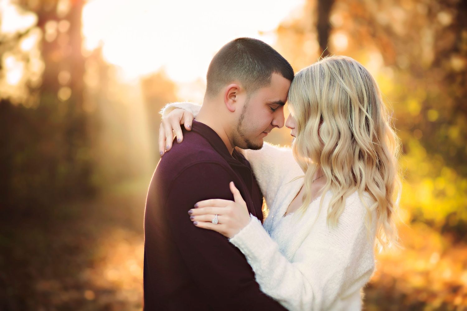 Couple sharing a romantic embrace outdoors in autumn golden hour light, surrounded by fall foliage.